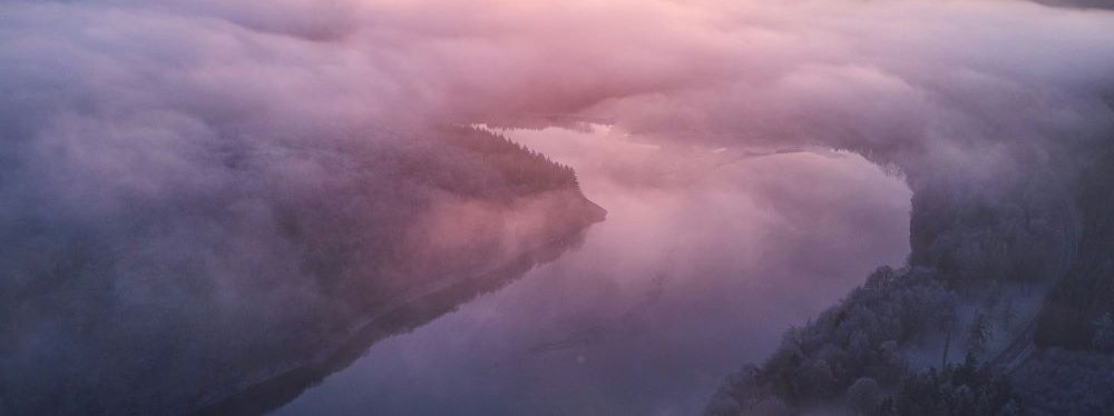 A valley with a winding river and low level clouds as the sun is setting.